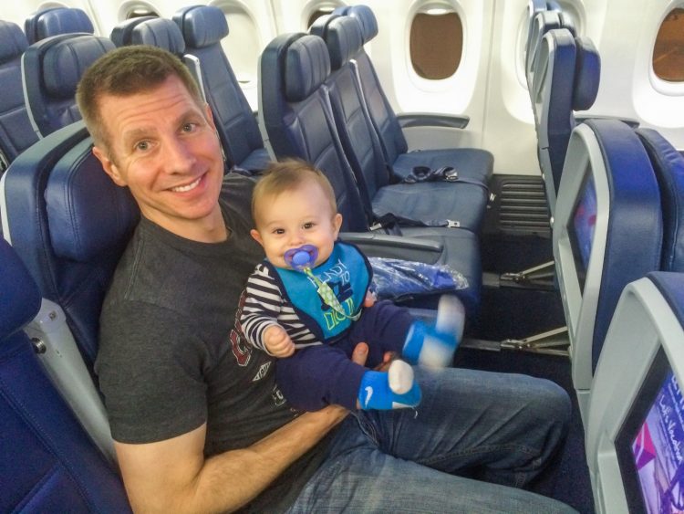 Man holding his baby with a smile on his face while sitting on a plane