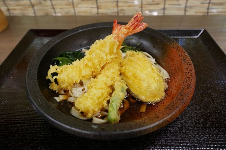 deep fried shrimp and vegetables on a bowl of soup with udon noodles. 